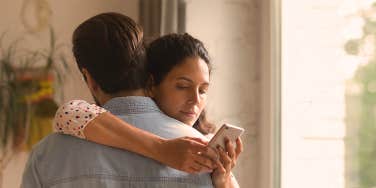 and woman and a man hugging, woman looking at her phone