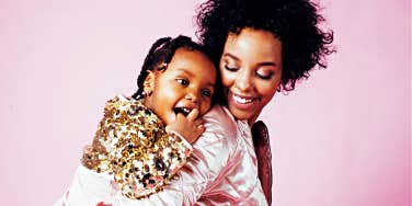 pretty young mom smiling at preschool daughter on her back, with a pink background