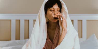 Woman covered by blanket, drinking wine 