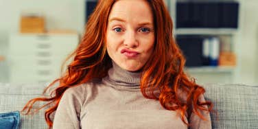 Pretty young redhead woman pulling a funny face making an exaggerated grimace with her lips as she sits on a sofa at home