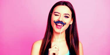 smiling woman holding up prop mustache to her face