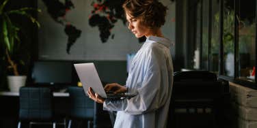concentrated business woman using laptop while standing in modern workspace