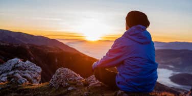 man sitting on top of mountain at sunset