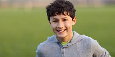 Young teen boy with dimples and black hair smiles in a grassy field