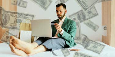 Man sitting in bed surrounded by bags and money online shopping