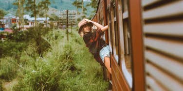  young woman hanging off the side of a train in the countryside