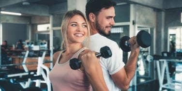 man and woman lifting weights at gym smiling