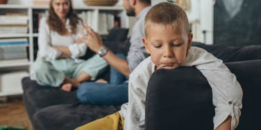 sad little boy with parents arguing behind him