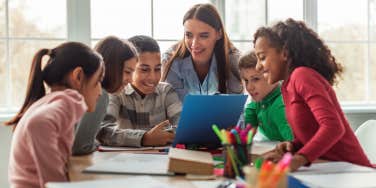 teacher with group of students working on schoolwork sitting around table in classroom