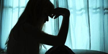 woman in shadow with hand on forehead