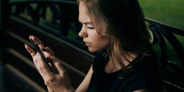 Young beautiful woman is sitting in the phone on a park bench in summer.