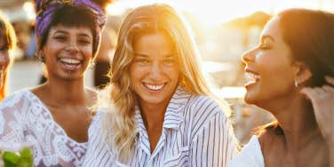 three women with a glowing sunset behind, laughing