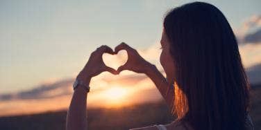 woman making a heart in the sunset