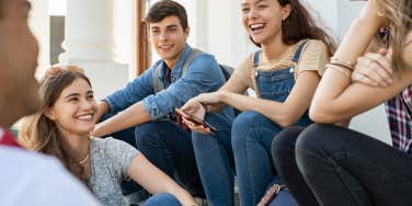 group of high school students sitting and laughing together outside