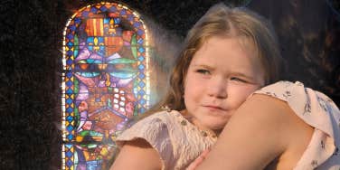 Young girl hugging her mother, reunited, church stained glass 