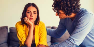 man and woman sitting on the couch, he is trying to get her to talk to him