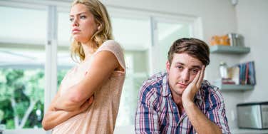 annoyed woman in the kitchen with her back to husband looking resigned