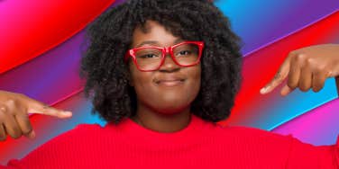 woman in red top in front of colorful background pointing to herself