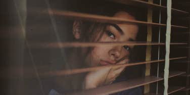 Woman looking sadly out her blinds 