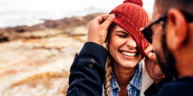 woman smiling while boyfriend affectionately plays with her beanie