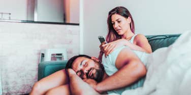 woman looking through phone next to sleeping man