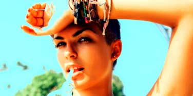 woman with one arm over her head drinking from a straw