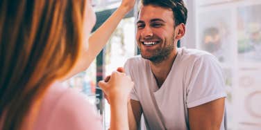 Joyful laughing romantic man in love holding hand of partner during flirting and showing care with tenderness while girlfriend touching hair