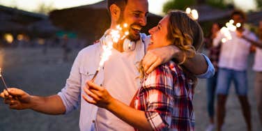 happy couple lighting sparklers at beach during sunset