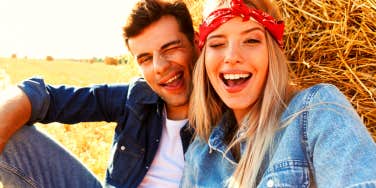 guy and girl sitting on hay stack smiling and winking at the camera
