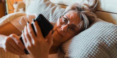 old woman looking at phone in bed