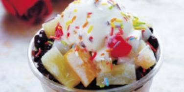 bowl of ice cream with a lot of toppings on table with roses