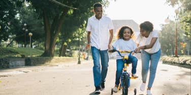 Parents helping kid ride a bike 