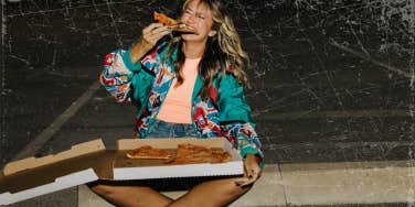 Woman eating pizza on a curb
