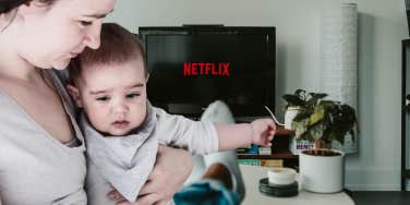 woman holding baby and man watching netflix