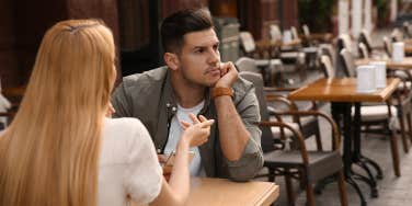 Man getting bored during first date with overtalkative young woman at outdoor cafe