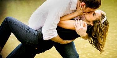 man dipping woman into a kiss by water