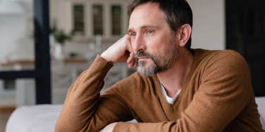 depressed man with hand on head looking out window