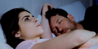 upset woman in bed with sleeping husband
