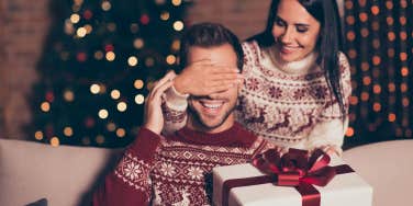 Woman covering boyfriends eyes while holding a holiday gift