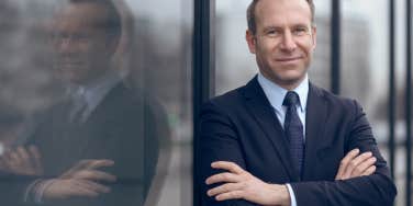 male businessman in blue suit and necktie with grin leaning on window outdoors