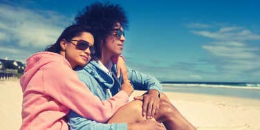 Latino couple on a beach, looking at the water, woman's arms around the man