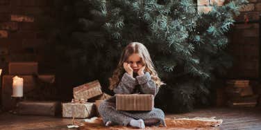 Sad kid sitting in front of an undecorated Christmas tree. 