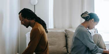 man and woman sitting back to back on a bed