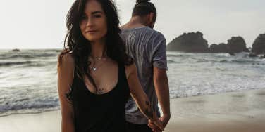 woman holding man's hand on beach as he walks away