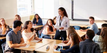 High School Teacher Standing By Student Table Teaching Lesson