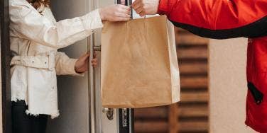 A food delivery driver is handing food to a woman.