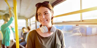 young woman wearing headphones around neck smiling on a tram