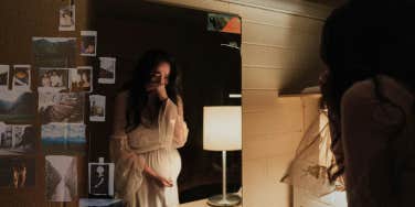 Pregnant woman looking in mirror, crying