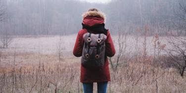 woman faces away from camera in misty, cold field wearing a red coat