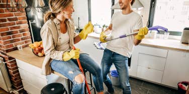 Couple in the kitchen cleaning, playing band with the cleaning tools